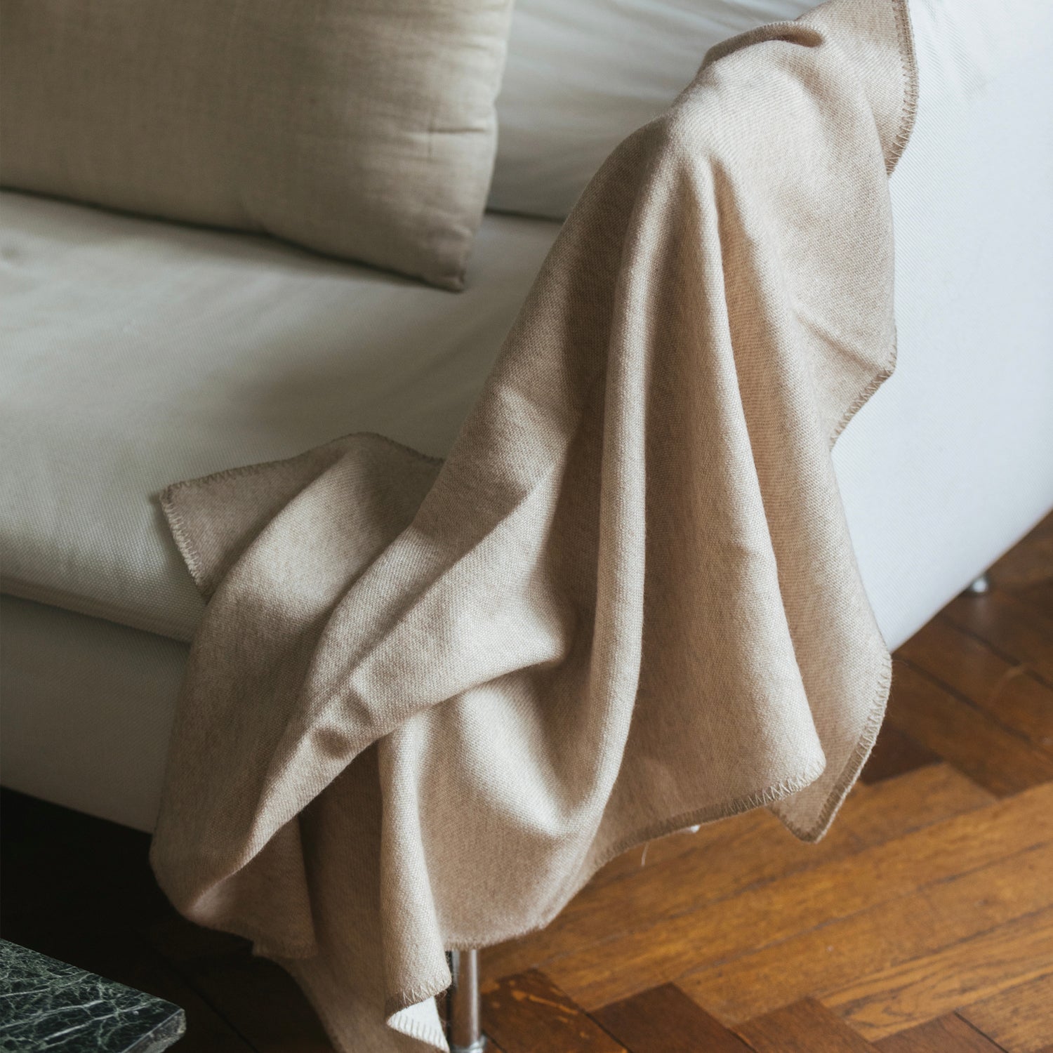 Beige merinoullfilt från Skogen Baby draperad över en soffa, elegant och mjuk för både barn och vuxna.