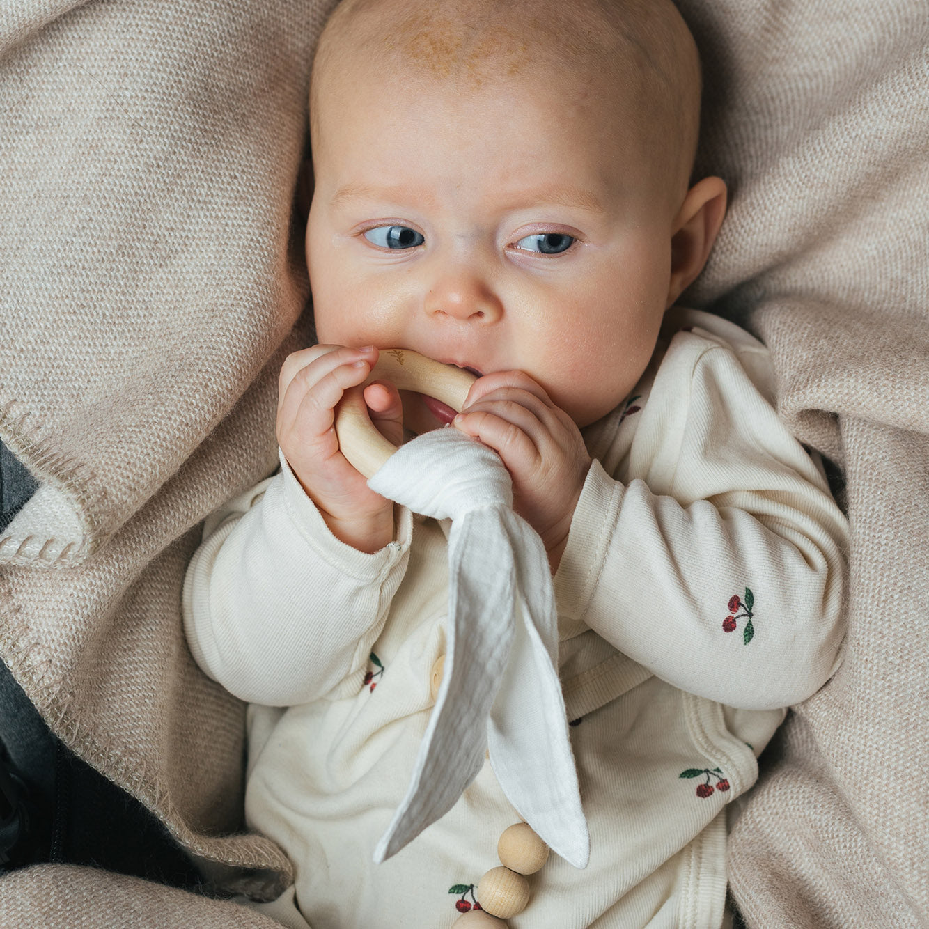 Bebis som biter på en naturlig träbitring med tygdetalj från Skogen Baby, insvept i en mjuk merinoullfilt.