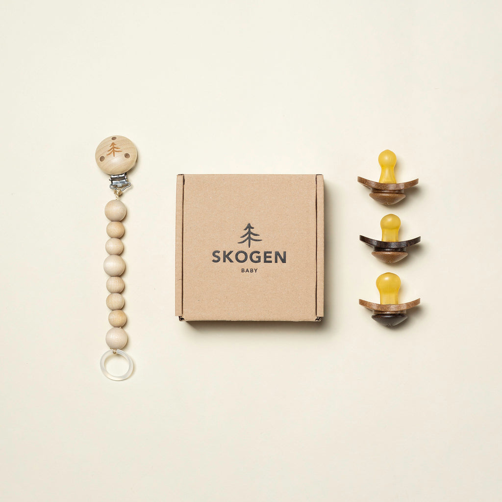 Skogen Baby presentförpackning som innehåller en naturlig napphållare i trä och tre ekologiska nappar tillverkade av förnybara material.