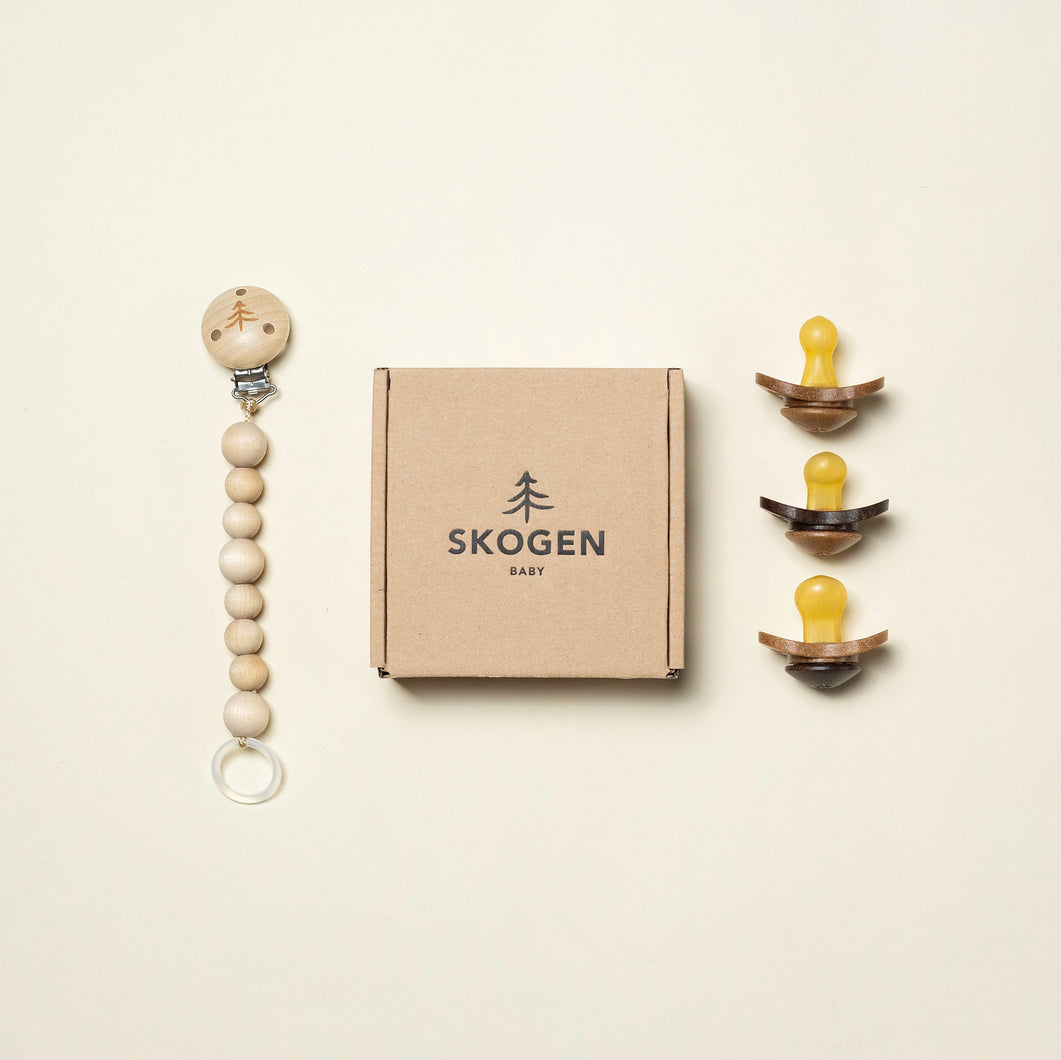 Skogen Baby presentförpackning som innehåller en naturlig napphållare i trä och tre ekologiska nappar tillverkade av förnybara material.