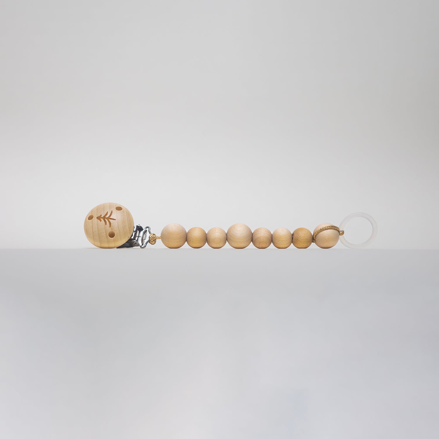 Naturlig napphållare i trä med minimalistisk design från Skogen Baby, perfekt för att hålla nappen nära och säker för små barn.